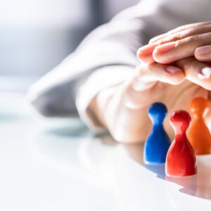 A pair of hands gently shelters a group of colorful game pieces, symbolizing protection and leadership.