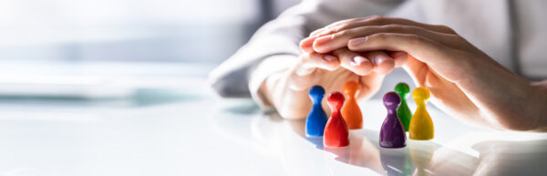 A pair of hands gently shelters a group of colorful game pieces, symbolizing protection and leadership.