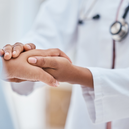 A doctor gently holds a patient’s hand, offering comfort and care during a medical consultation.